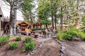 Un lodge rústico con mobiliario exterior, un camino de piedra y un bosque natural de fondo.
