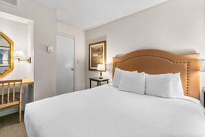 A hotel room with a large bed, a wooden headboard, a desk with a chair, a mirror, and a painting on the wall.