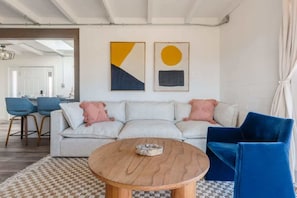 A modern living room with a sofa, a round wooden coffee table, and blue chairs. There are abstract paintings on the wall. - Kinetic House by Homestead Modern (Yucca Valley)