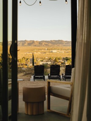 A room with a view of a desert landscape, featuring two black lounge chairs and a small round ottoman.
