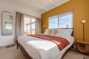 A modern bedroom with a large bed, a window with a view, a mirror, and a lamp. - Kinetic House by Homestead Modern (Yucca Valley)