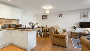 A modern living room with a sofa, a dining table, and a kitchen area with white cabinets and a wooden countertop.