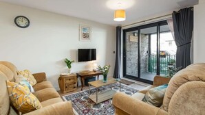 A living room with a sofa, a coffee table, a TV, and a sliding glass door leading to a balcony.