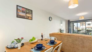 A dining area with a wooden table set for two, a bowl of fruit, and a clock on the wall.