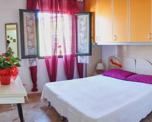 Une chambre à coucher avec un lit, une table de chevet, une lampe, une fenêtre avec des rideaux et un miroir.