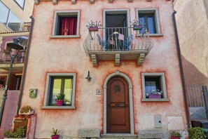 A building with a pink facade, a wooden door, and multiple windows with potted plants. - Villa Rosa (Santa Teresa Gallura)