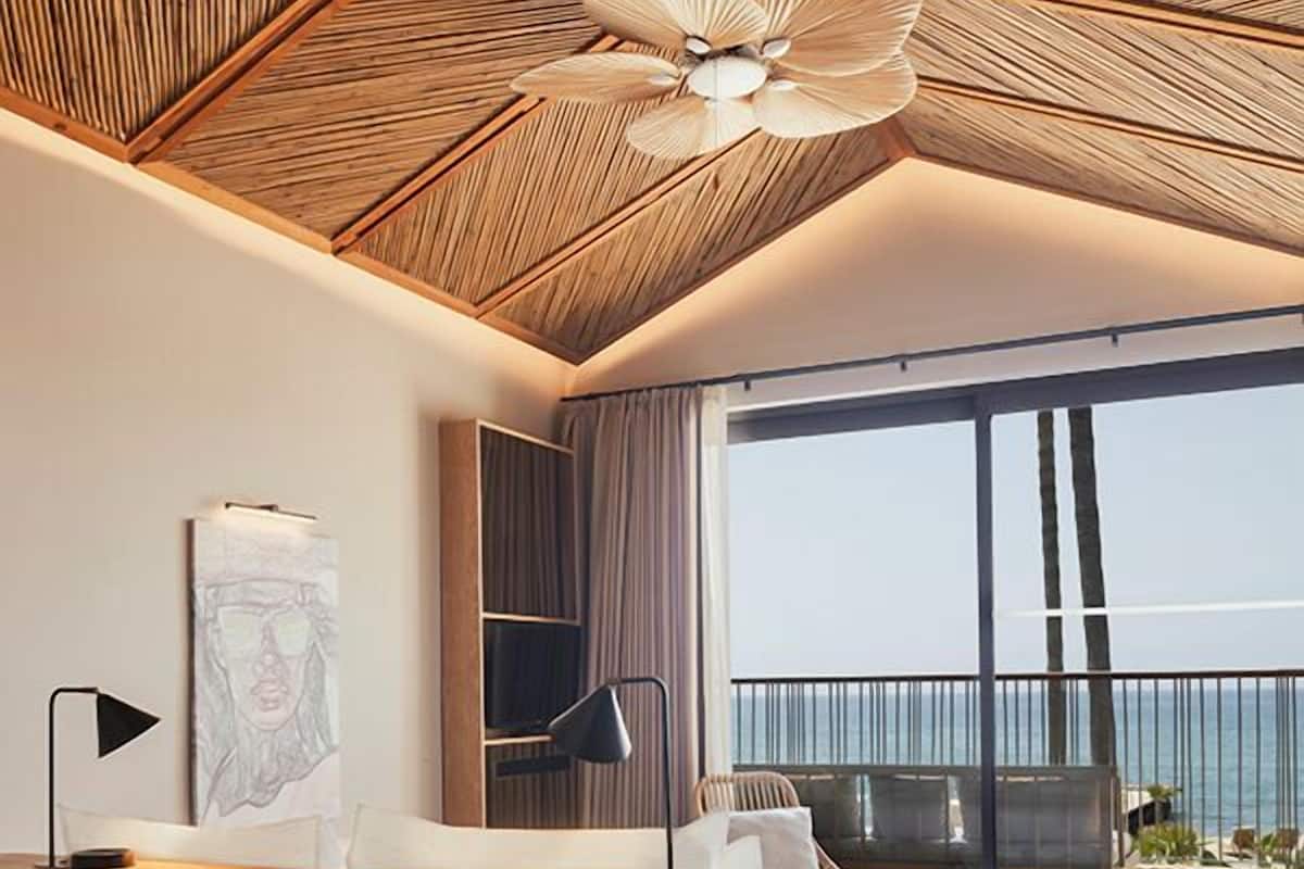 Une chambre d’hôtel moderne dotée d’un grand balcon, d’un plafond en bois et d’un lit offrant une vue sur la mer.