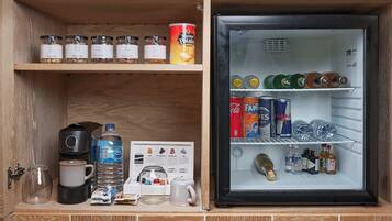 A compact kitchenette with a refrigerator containing beverages, a coffee maker, and a water dispenser.
