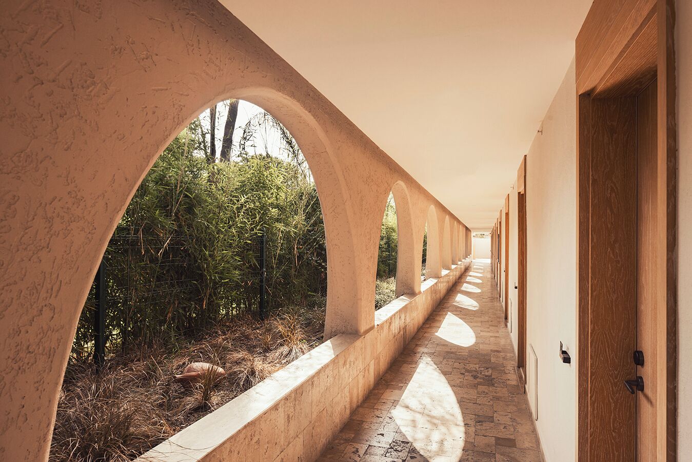A corridor with arches, a pathway, and wooden doors.
