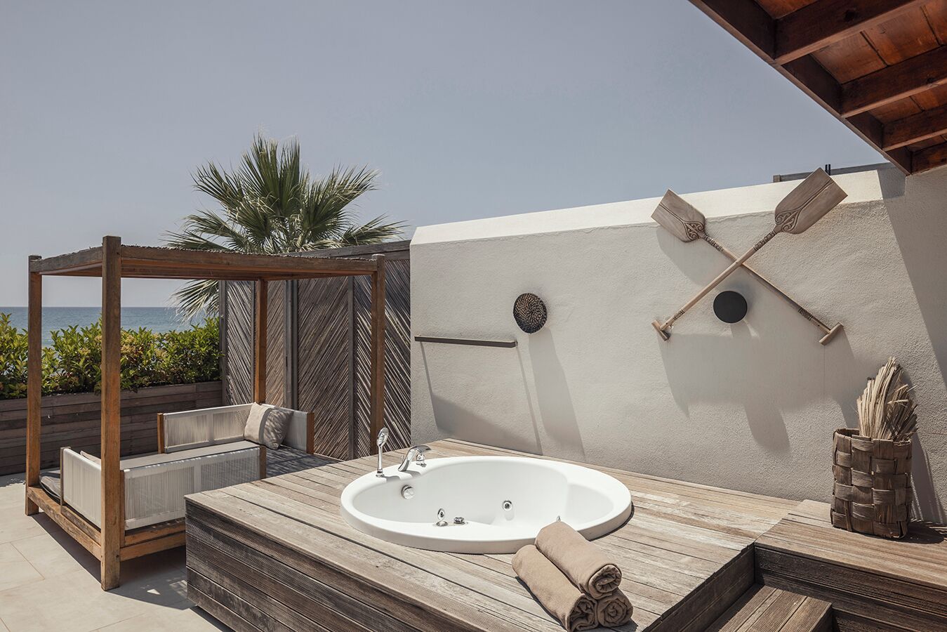 A rooftop outdoor bathroom with a hot tub, wooden deck, and a pergola with seating.