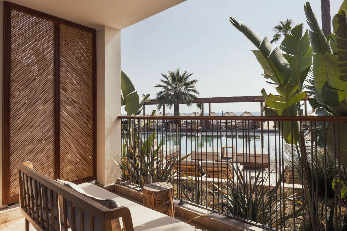 Un balcon donnant sur une piscine, entouré de plantes tropicales et délimité par une clôture en bois.
