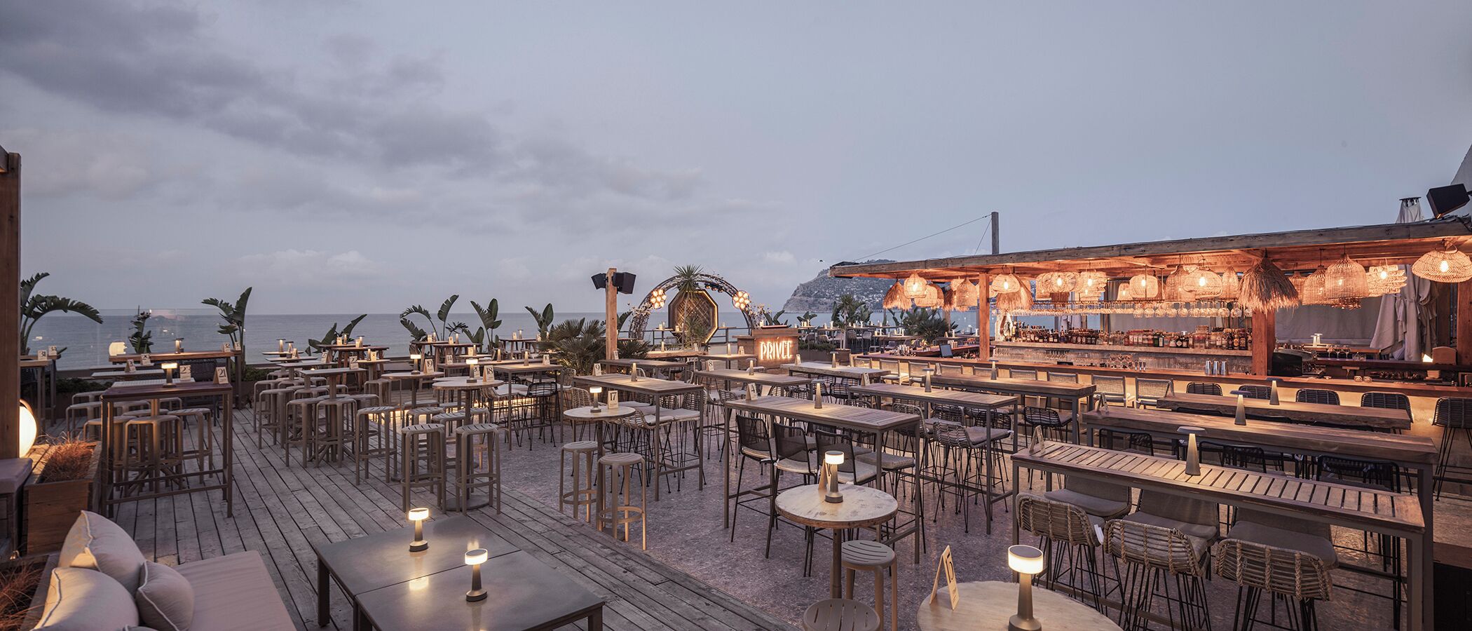 Un bar situé sur le toit, avec de nombreuses tables et chaises, un espace bar et une vue sur l’océan.