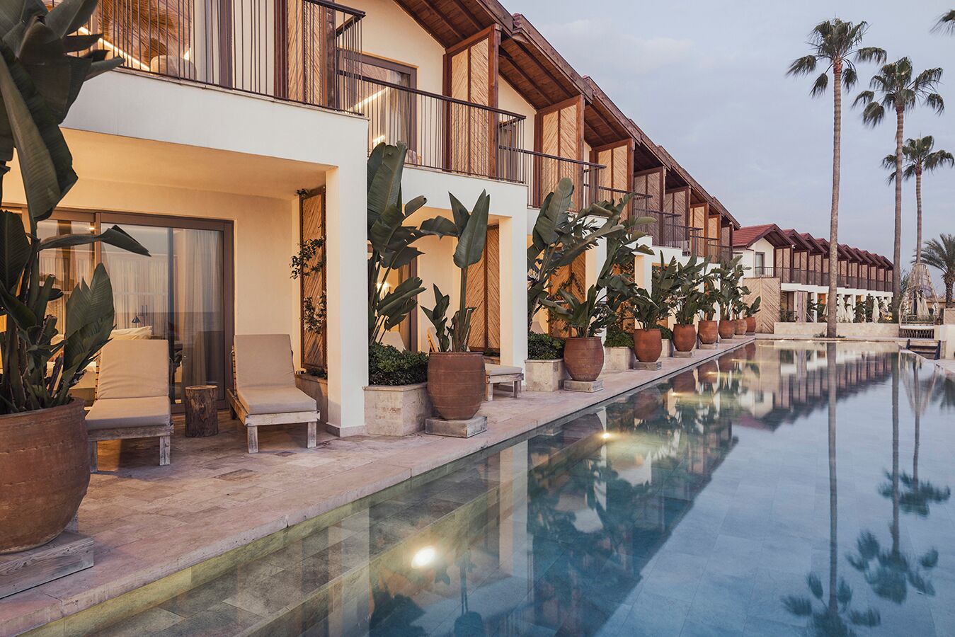 A hotel with a pool, outdoor seating, and tropical plants.