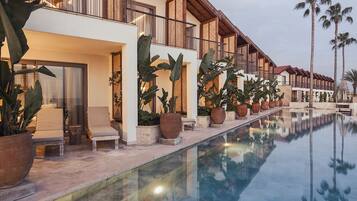 A hotel with a pool, outdoor seating, and tropical plants.