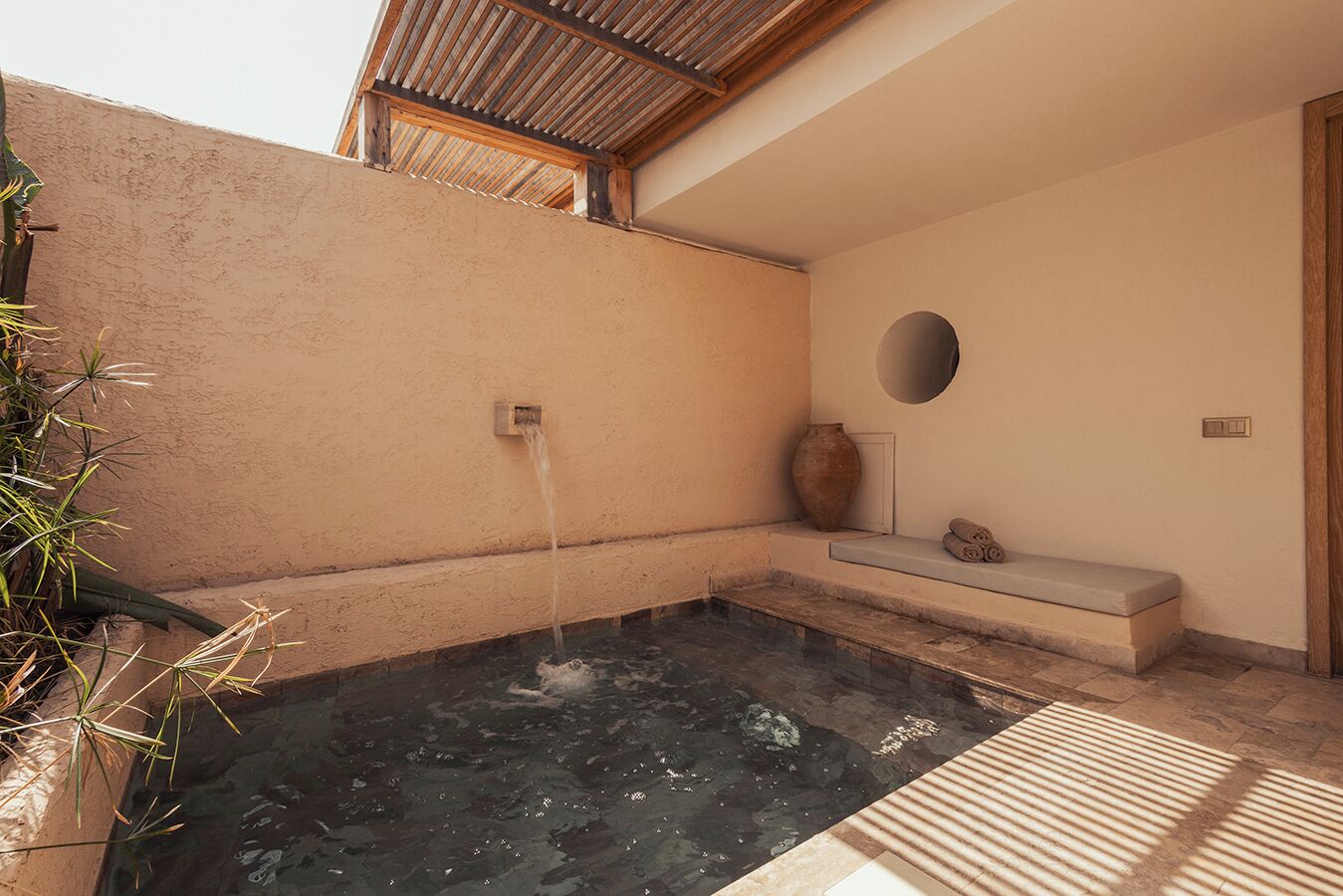 A spa area with a hot spring, a wooden bench, a vase, and a wall-mounted light fixture.