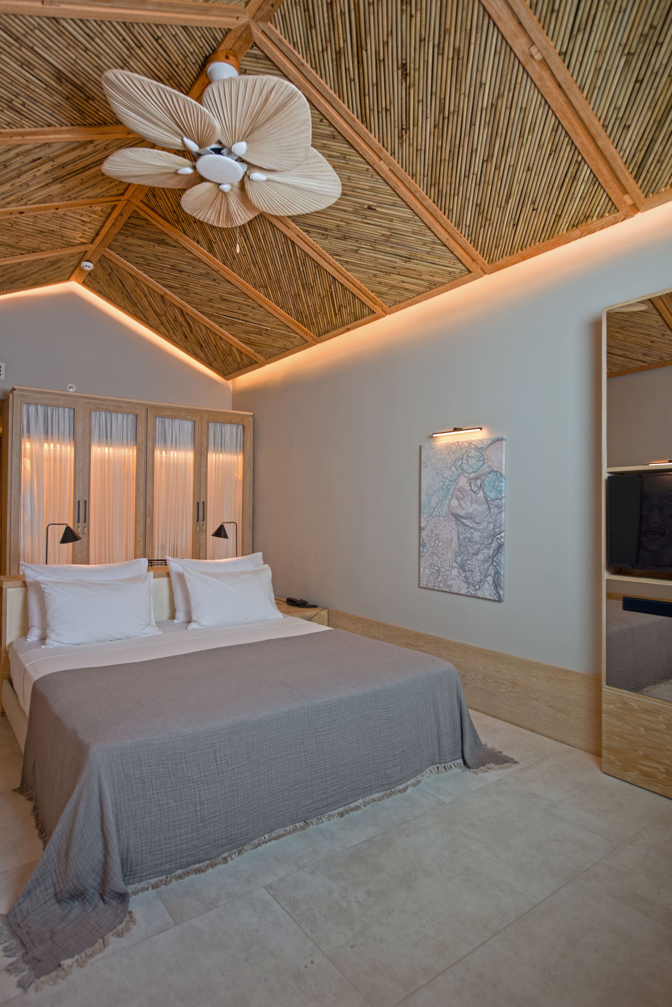 Quarto com cama, luminárias de cabeceira, ventilador de teto e uma obra de arte na parede.