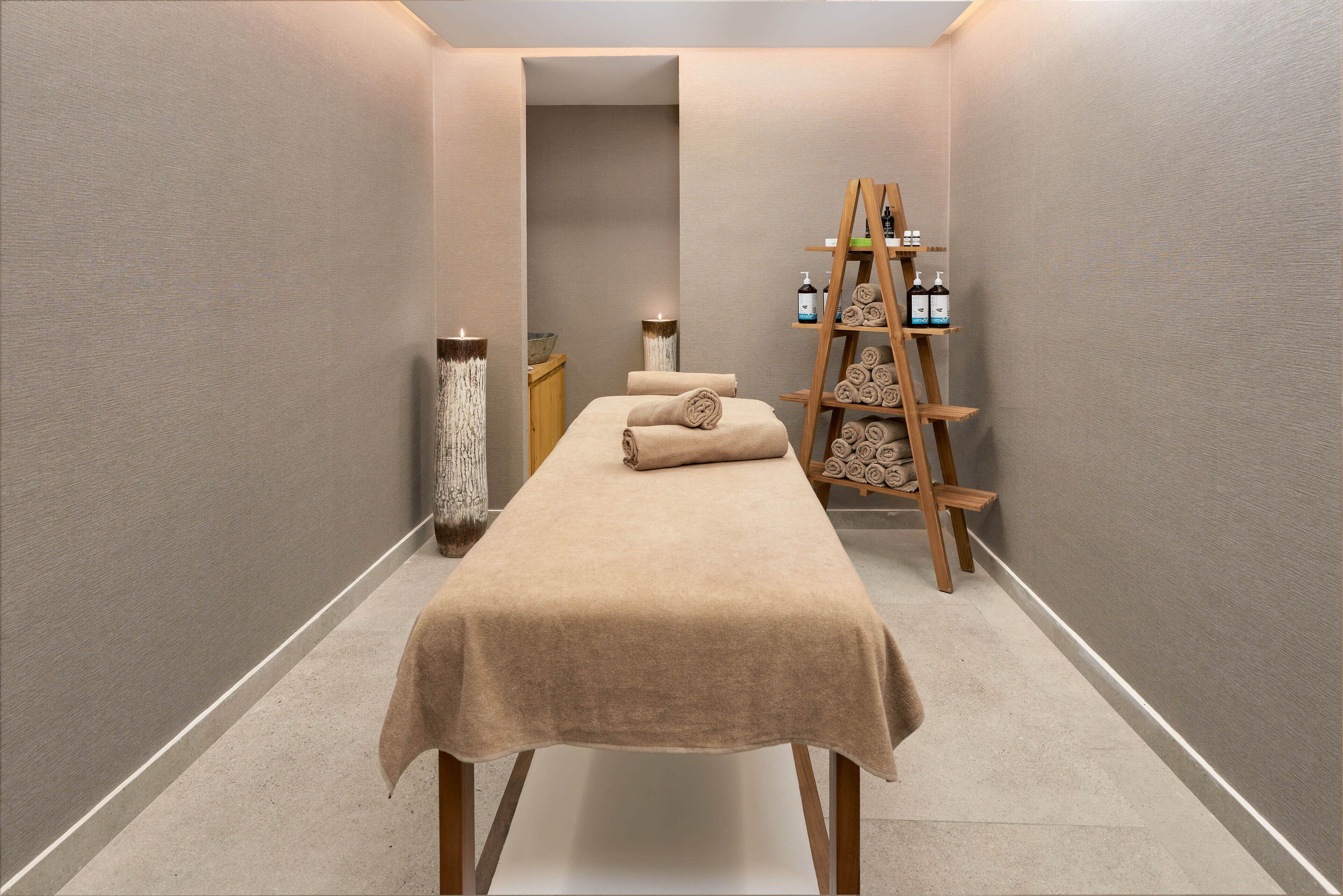 Ein Spa-Raum mit Massagetisch, Kerzen und einer Holzleiter-Regal mit Flaschen.