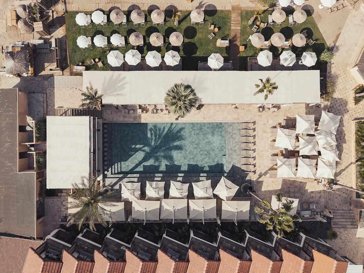 An aerial view of a resort with a swimming pool, sun loungers, and umbrellas.