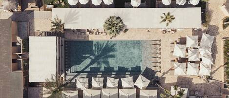 An aerial view of a resort with a swimming pool, sun loungers, and umbrellas.