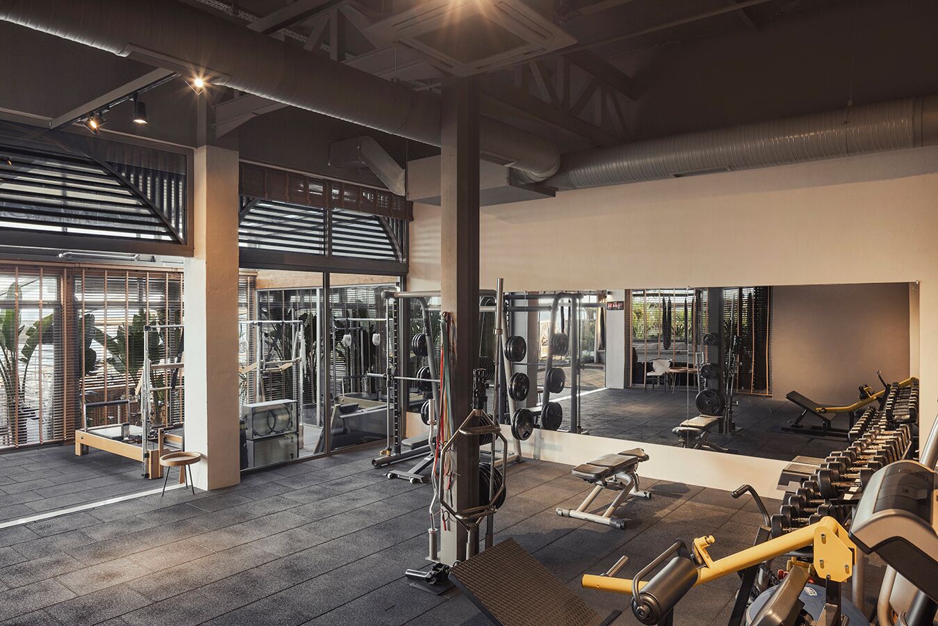 A spacious gym with various exercise equipment, large windows, and a high ceiling.