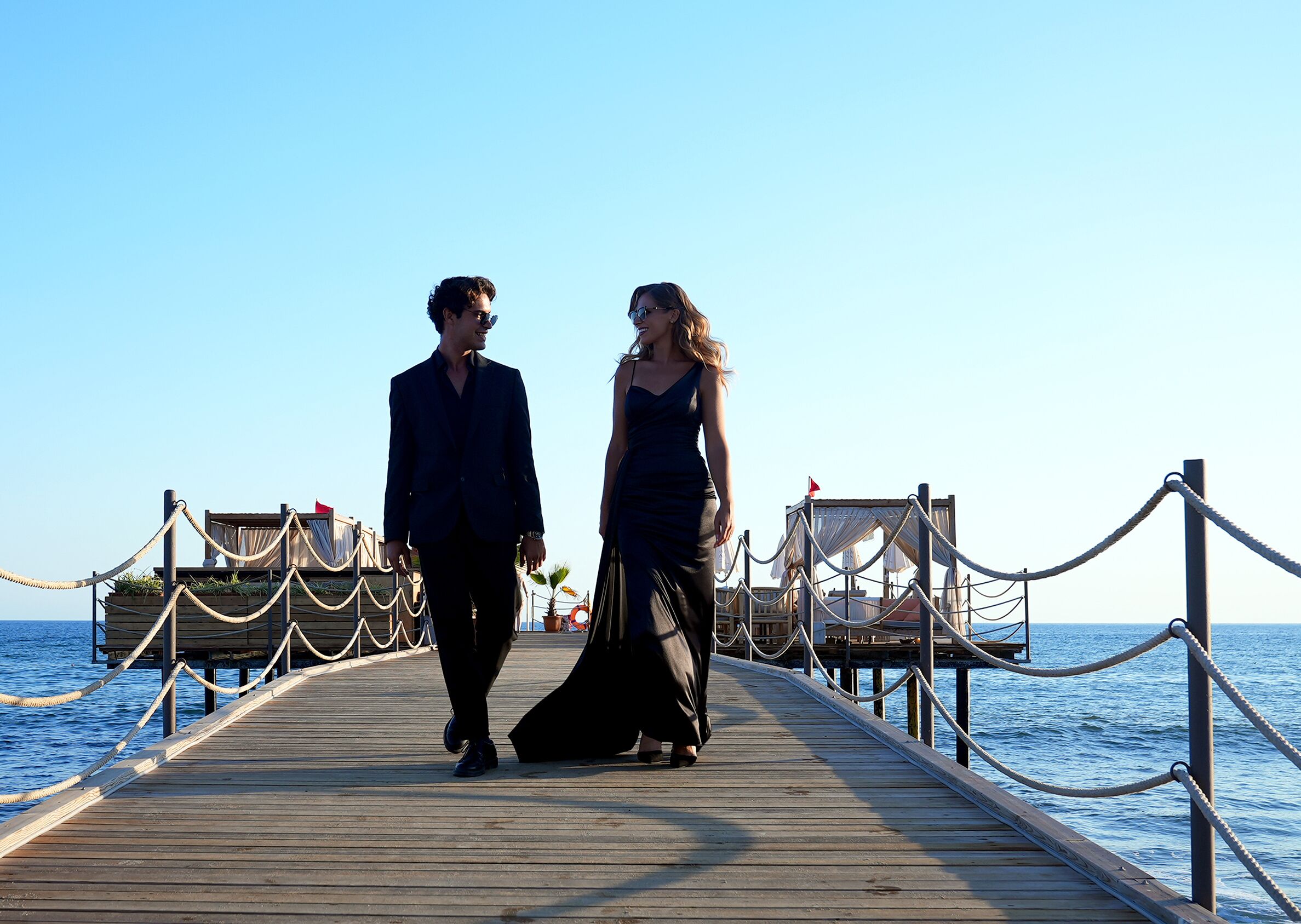 A wooden pier extending into the sea with a couple walking along it.