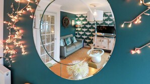 A living room with a circular mirror, teal walls, a grey sofa, a white coffee table, and a TV.
