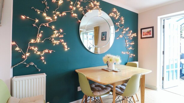 A dining area with a round table, two chairs, a mirror, and string lights on the wall.