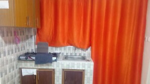 A small kitchen with a sink, cabinets, and a red curtain. - Stay.Plus Utawala Studio Apartment (Nairobi)