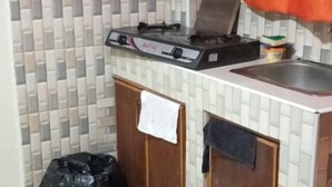 A small kitchen with a gas stove, cabinets, a tiled backsplash, and a black rug on the floor. - Stay.Plus Utawala Studio Apartment (Nairobi)
