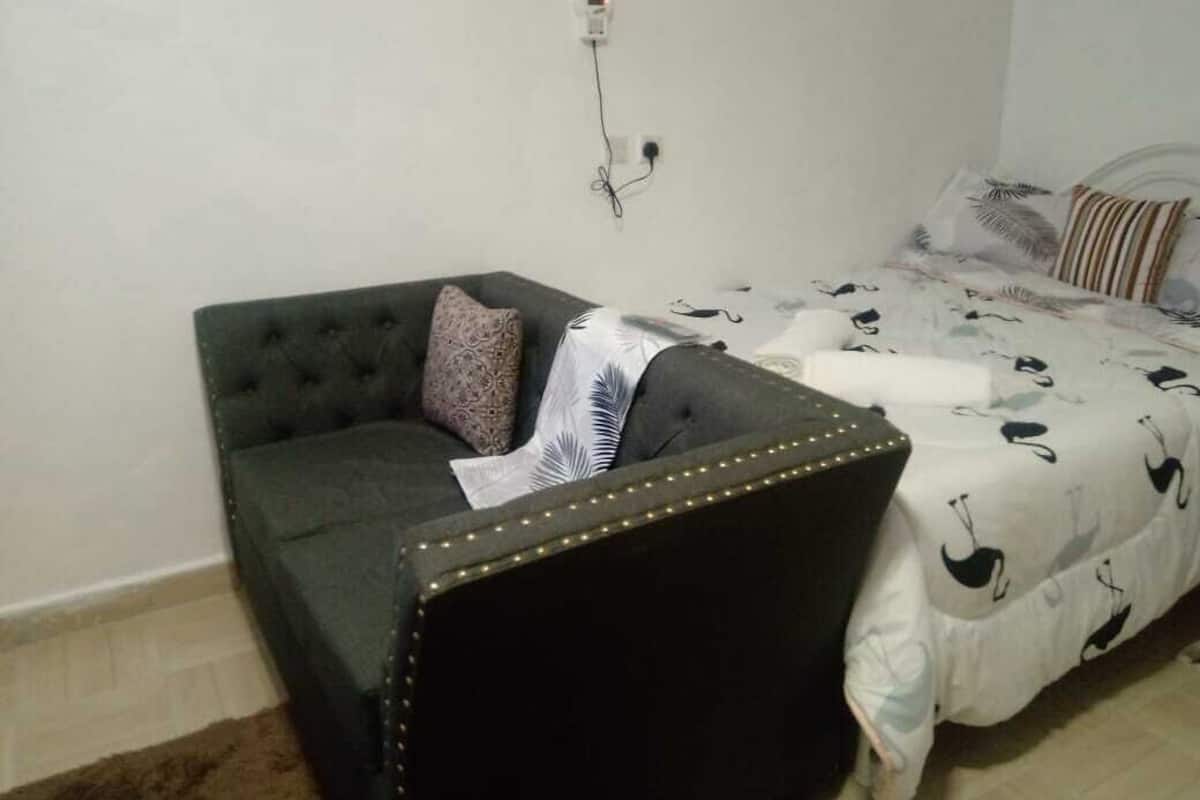 A room with a dark green sofa, a patterned pillow, and a bed with a white bedspread featuring black bird patterns.