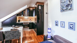 A modern kitchen with dark cabinetry, a dining area with patterned chairs, and a living area with a sofa and wall art. - Central & Typical Lisboa by GT House (Lisboa ciudad)