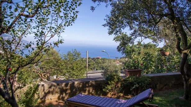 Un fauteuil de jardin en bois, placé dans un jardin offrant une vue sur la mer et les collines.