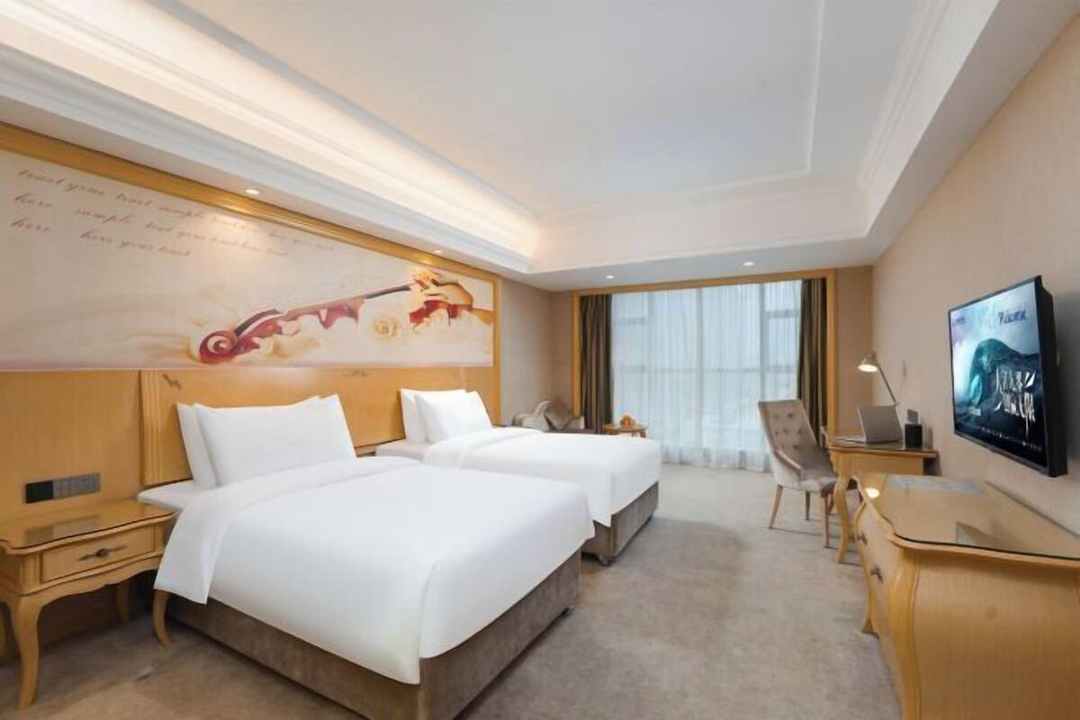 A hotel room with two beds, a desk, a chair, a TV, and a large window.