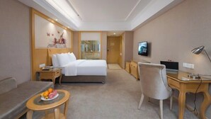 Habitació d'hotel amb un llit, una taula de treball, una cadira, una televisió i una taula petita amb fruita.