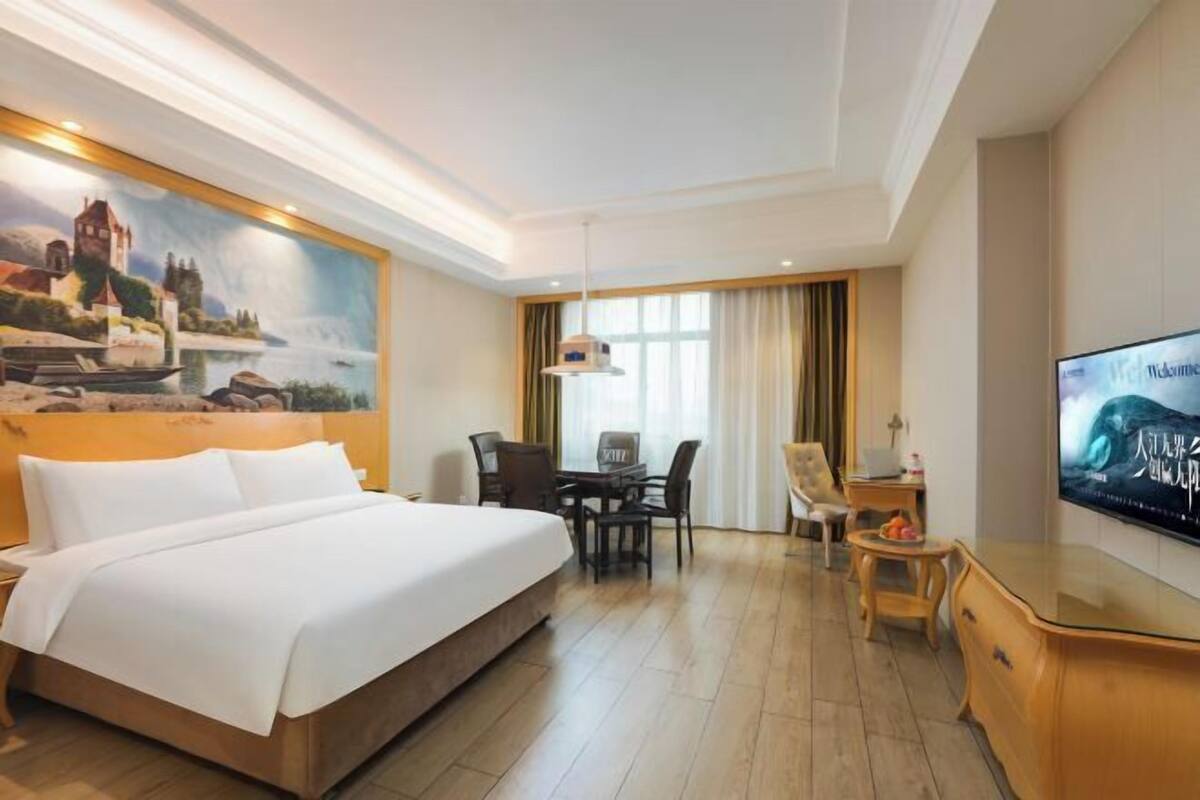 A hotel room with a bed, a desk, a chair, a television, and a painting on the wall.