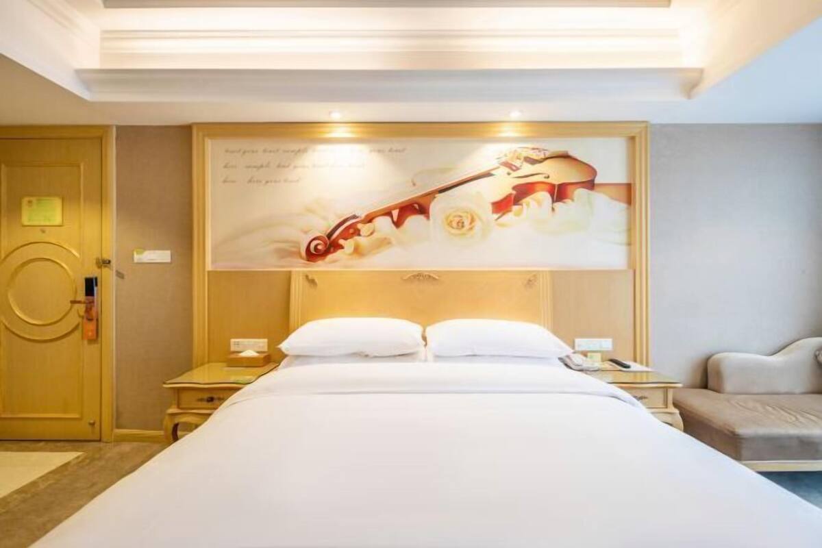 A hotel room with a bed, a bedside table, a nightstand, a lamp, a wall-mounted artwork, and a door.