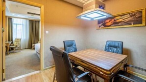 Habitació d'hotel amb taula de dinar de fusta, cadires de pell negra, un quadre a la paret i un llit amb cortines.