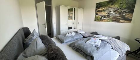 Habitación de hotel con una cama grande, ropa de cama gris, un plaid suave, un armario y un cuadro de un paisaje.