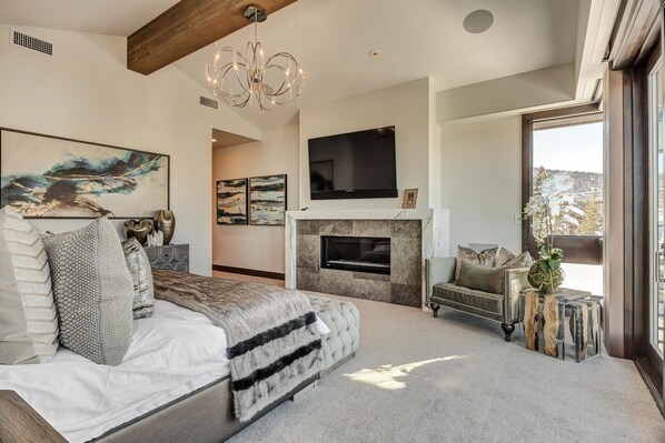 Un dormitorio amplio con una cama grande, una chimenea, un televisor montado y vistas al exterior.