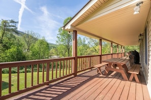 A wooden deck with a covered area, picnic tables, and a barbecue grill.
