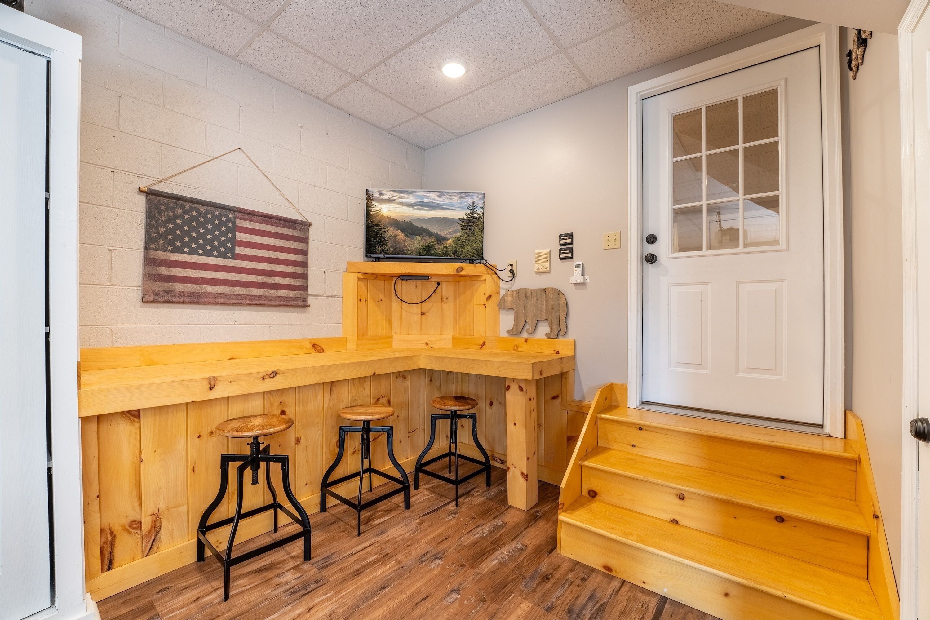 A wooden bar area with stools, a painting of a landscape, and an American flag.