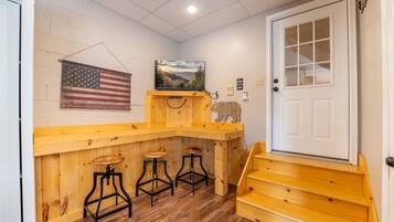 A wooden bar area with stools, a painting of a landscape, and an American flag.