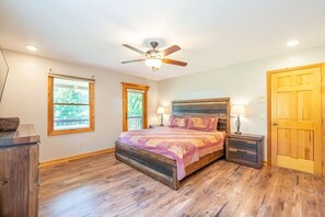 A bedroom with a wooden bed, two windows, a ceiling fan, and a wooden door.