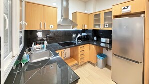 Una cocina moderna con encimeras de mármol negro, electrodomésticos de acero inoxidable, armarios de madera y horno empotrado.
