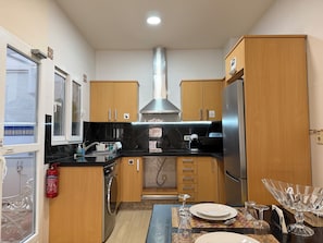 Eine Küche mit Holzausstattung, einem Edelstahl-Kühlschrank, einer Waschmaschine und einem Essbereich mit Tisch für zwei Personen.