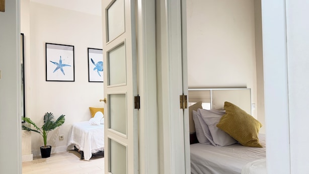 Una habitación con una cama, una mesita de noche, una planta en maceta y dos cuadros en la pared.