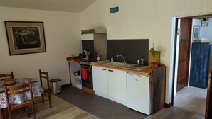 A compact kitchen with a stove, sink, and cabinets, a dining area with a table and chairs, and a painting on the wall. - Charming Gîte (4 people) ideal for couples or families, near Montcuq
 (PORTE DU QUERCY)