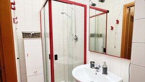 A compact bathroom with a glass-enclosed shower, a white sink, and a washing machine. - Casa Mirtillo (Turin)