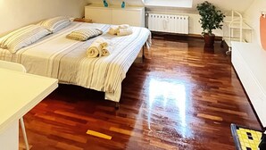 A bedroom with a sloped ceiling, a bed with striped bedding, a bedside table, a radiator, a window with a curtain, and a potted plant. - Casa Mirtillo (Turin)