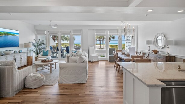 A spacious living area with a large TV, white furniture, and a view of the ocean.